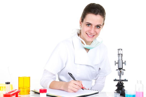 Serious  female scientist using microscope and writing in note pad  - Photo, Image
