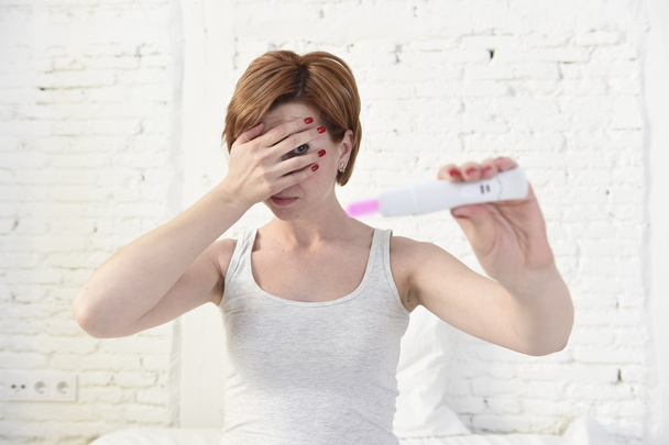 έγκυος γυναίκα κρατώντας ροζ θετικό τεστ εγκυμοσύνης καλύπτοντας τα μάτια της με το χέρι της - Φωτογραφία, εικόνα