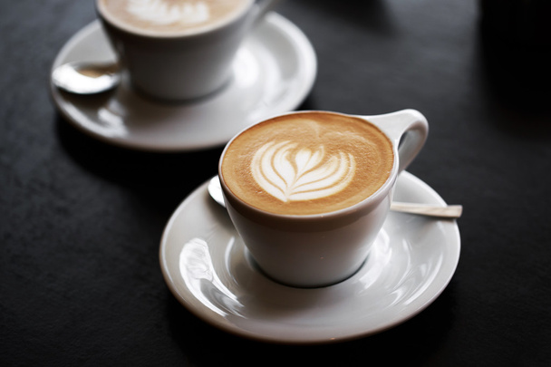 Two cups of cappuccino on black table - 写真・画像