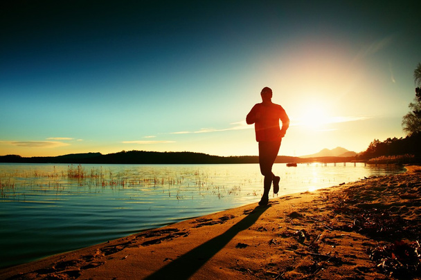 Силуэт спортивного активного мужчины бегущего и упражняющегося на пляже на закате
. - Фото, изображение