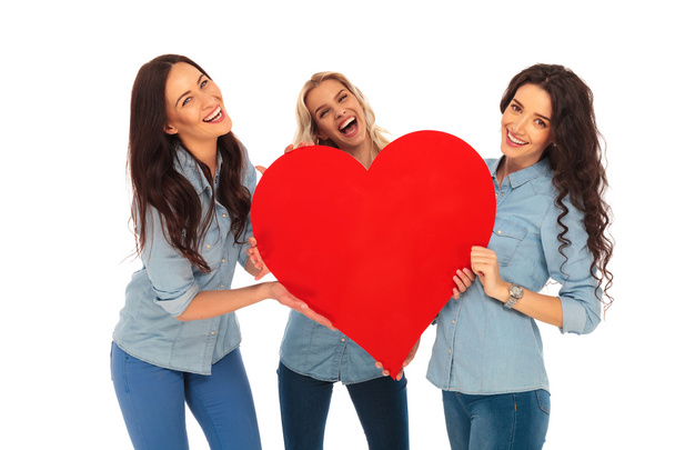 três mulheres casuais rindo segurando um grande coração vermelho
 - Foto, Imagem