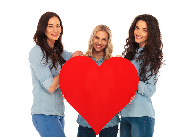 3 mulheres sorrindo oferecendo seu grande coração vermelho para você
 - Foto, Imagem
