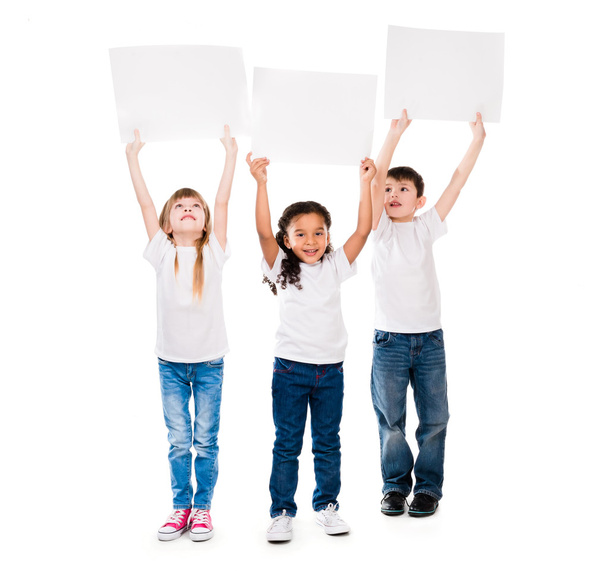 kolme hilpeää lasta, jotka pitävät tyhjää paperiarkkia yläpuolellaan
 - Valokuva, kuva