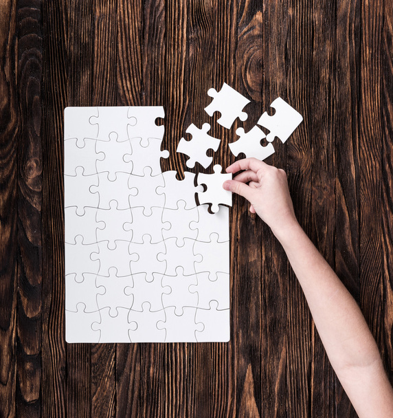 hand collecting white puzzle on brown background - Photo, image