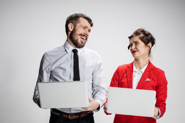 The young businessman and businesswoman with laptops  communicating on gray background - Foto, Bild