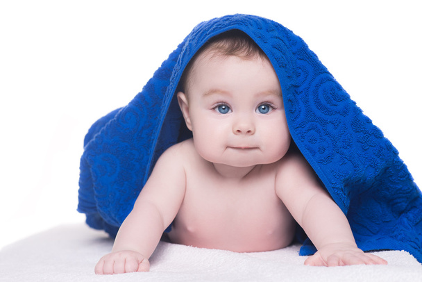 bebé con grandes ojos azules mirando a la cámara bajo la toalla azul / en blanco
 - Foto, Imagen