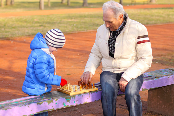 Opa en kleinzoon spelen schaak buitenshuis - Foto, afbeelding