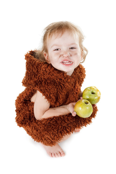 Piccolo divertente ragazzo di Neanderthal in un vestito con la faccia sporca mangiare una mela
.  - Foto, immagini