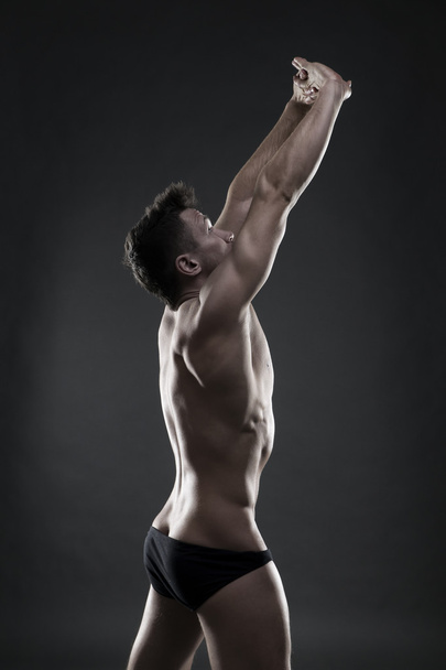 Handsome muscular bodybuilder posing on gray background. Low key studio shot - Foto, immagini