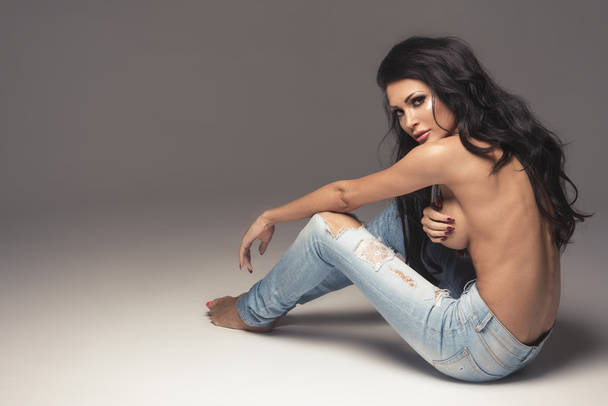 Sexy attractive brunette woman posing only in jeans in studio - Фото, зображення