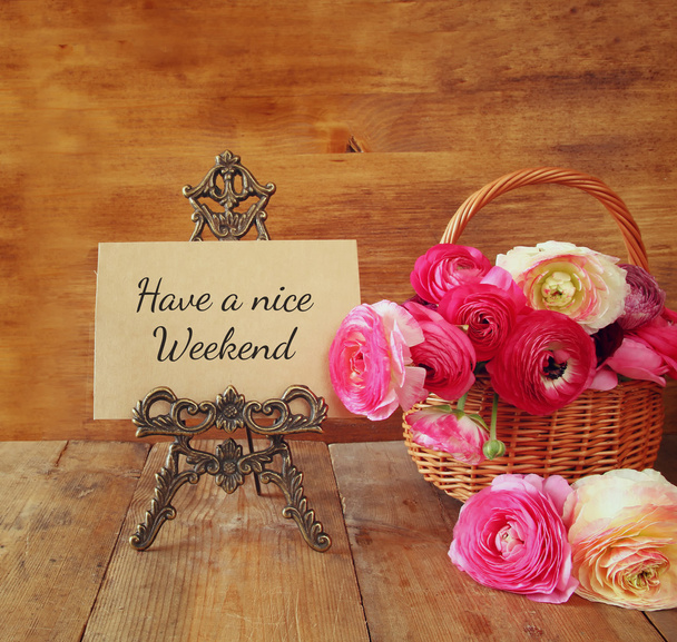 pink flowers in the basket next to card with phrase: HAVE A NICE WEEKEND, on wooden table - Photo, image