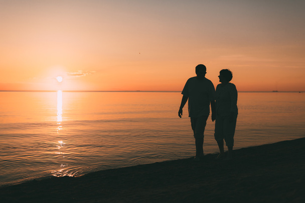 Silhouette of adult couple walks on the seashore against a sunset. - Foto, immagini