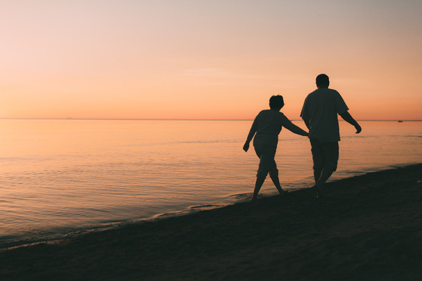 Silhouette of adult couple walks on the seashore against a sunset. - Φωτογραφία, εικόνα