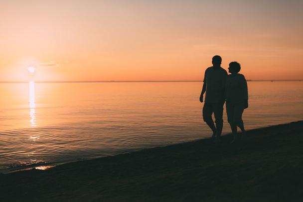 Silhouette of adult couple walks on the seashore against a sunset. - Fotoğraf, Görsel