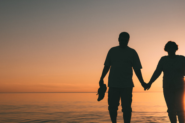 Silhouette of adult couple standing in the sea against a sunset. - Foto, imagen