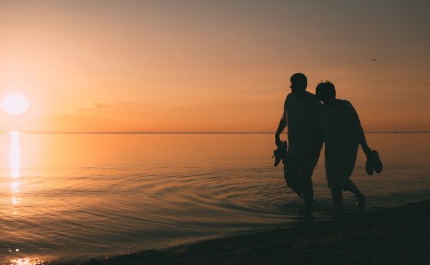 Silhouette of adult couple walks on the seashore against a sunset. - Fotoğraf, Görsel