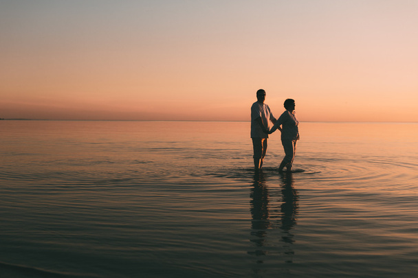 Silhouette of adult couple standing in the sea against a sunset. - Foto, immagini