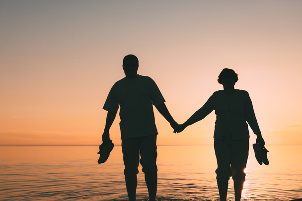 Silueta dospělého páru stojící v moři proti západu slunce. - Fotografie, Obrázek