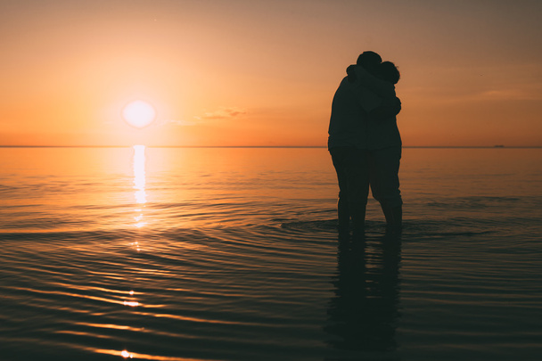 Silhouette of adult couple standing in the sea against a sunset. - Foto, afbeelding