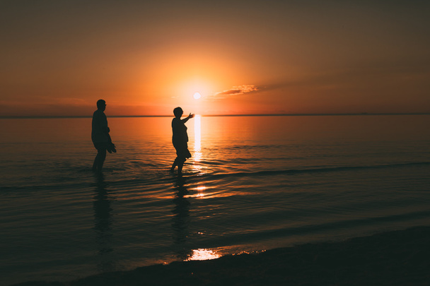 Silhouette of adult couple which costs in the sea and holds in hand footwear. - Foto, imagen