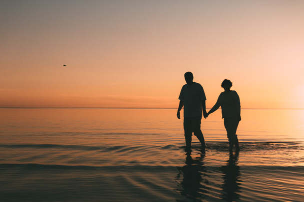 Silhouette of adult couple standing in the sea against a sunset. - Foto, Bild