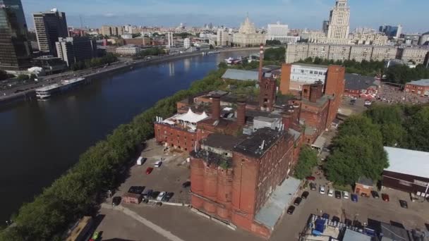 Quadrocopter vliegen rond oude bakstenen gebouwen met buizen in de stad aan de rivier. Zonnige zomerdag. Stadsgezicht - Video