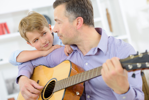 Man playing guitar, child leaning on his shoulder - Φωτογραφία, εικόνα