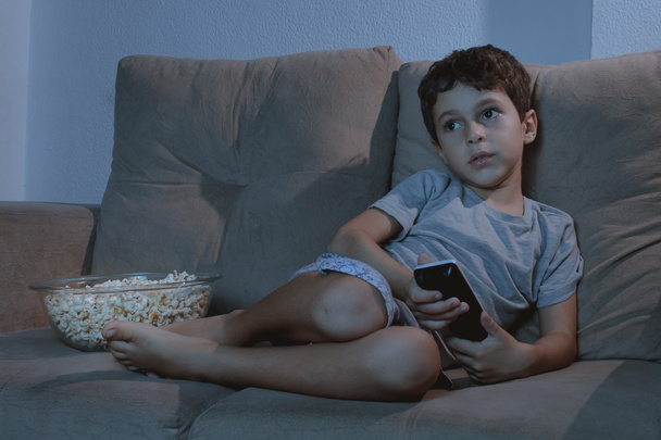 Mały chłopiec na kanapie przed telewizorem i jedzenie popcornu w nocy i - Zdjęcie, obraz
