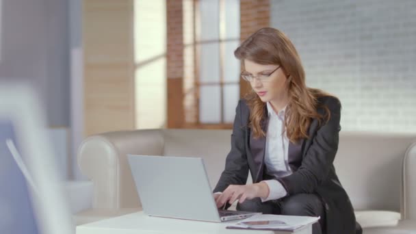 Beautiful woman office employee typing on laptop, smiling at cam - Felvétel, videó