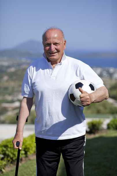 Un giocatore di calcio anziano con bastone da passeggio in possesso di un pallone da calcio
 - Foto, immagini