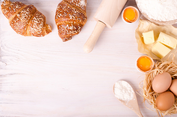 Ingredients for baking croissants - flour, wooden spoon, rolling pin, eggs, egg yolks, butter served on white background. - Photo, image