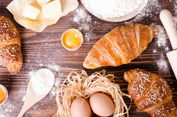Ingredients for baking croissants - paper, flour, wooden spoon, rolling pin, eggs, egg yolks, butter served on a rustic wooden tray table.  - Photo, image