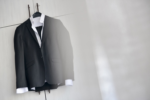 Black suit hanged to a wood closet in natural light - Photo, Image