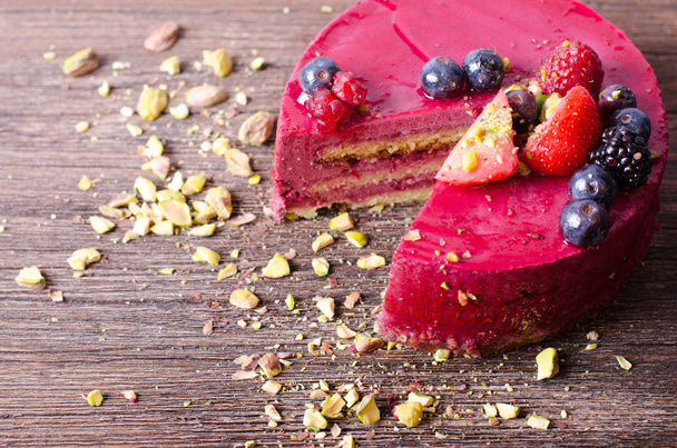 Delicious raspberry cake with fresh strawberries, raspberries, blueberry, currants and pistachios on wooden background.  - Photo, Image