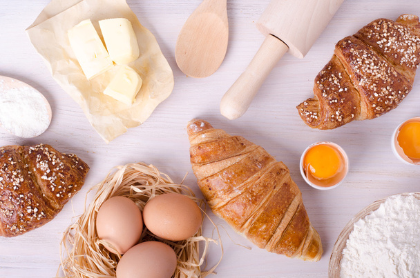 Ingredients for baking croissants - flour, wooden spoon, rolling pin, eggs, egg yolks, butter served on white background. - Foto, afbeelding