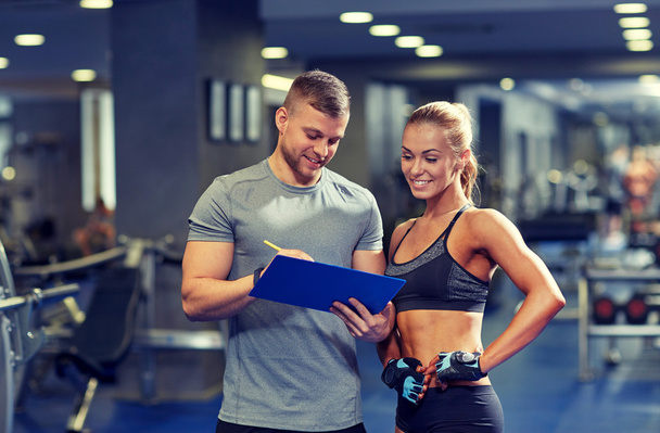smiling young woman with personal trainer in gym - Foto, immagini