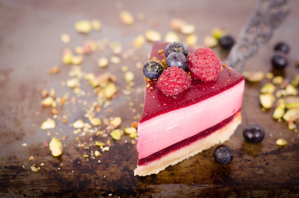 Piece of delicious raspberry cake with fresh raspberries, blueberry, currants and pistachios on shovel, black background. Free space for your text. - Foto, Imagem