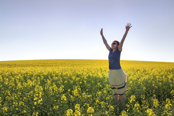 Chica feliz entre las plantas de canola bajo el cielo azul
 - Foto, imagen