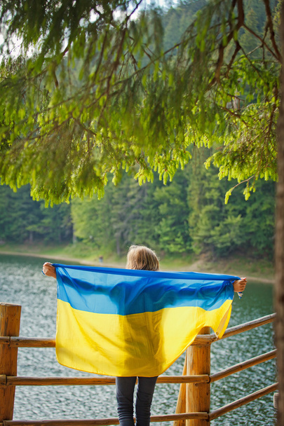 Young girl holding a flag of Ukraine on lake - Фото, изображение
