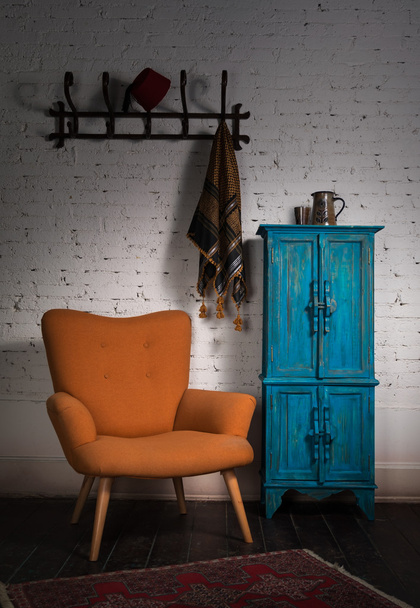 Παλιάς χρονολογίας πορτοκαλί πολυθρόνα, μπλε ντουλάπι, κρεμάστρα τοίχου και μαύρο κασκόλ - Φωτογραφία, εικόνα