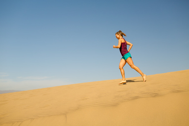 Νεαρή γυναίκα που τρέχει σε αμμόλοφους άμμου της ερήμου - Φωτογραφία, εικόνα