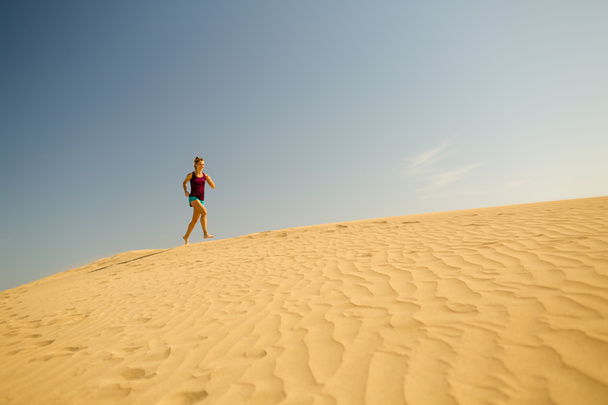 Νεαρή γυναίκα που τρέχει σε αμμόλοφους άμμου της ερήμου - Φωτογραφία, εικόνα