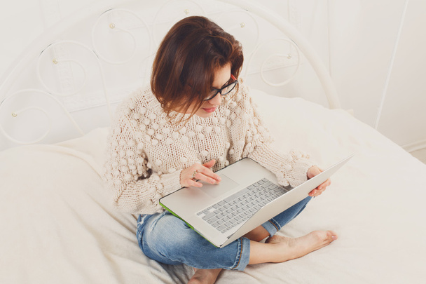 Jeune femme lit à partir d'un ordinateur portable au lit, clé haute
 - Photo, image