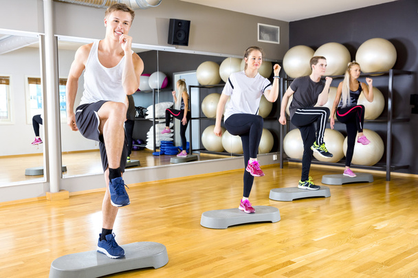 Grupo sorridente levantando pernas em plataformas de degrau no ginásio de fitness
 - Foto, Imagem