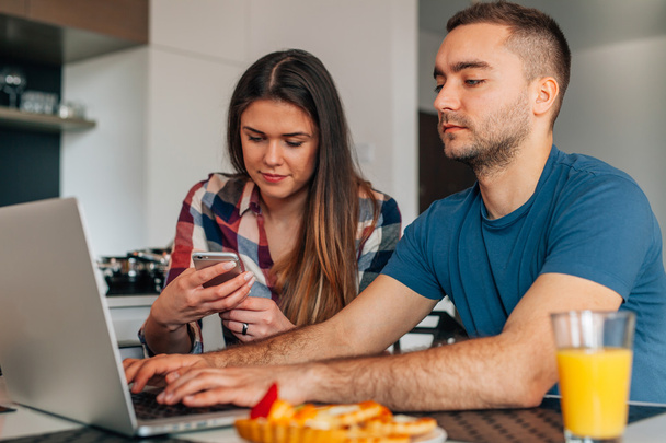 Young couple sitting in the kitchen. Man is using laptop. Girl i - Foto, imagen