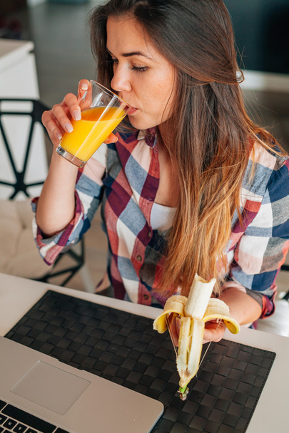 Fiatal nő ivás lé és étkezési banán, a konyhában.  - Fotó, kép