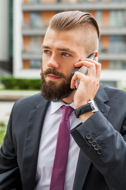 Young bearded businessman using mobile phone outside the office. - Fotoğraf, Görsel
