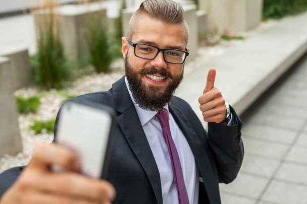Young happy bearded businessman standing outside office building - Foto, imagen
