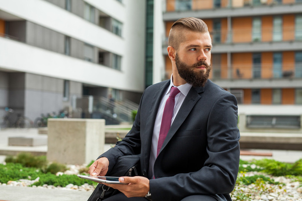 Young bearded businessman sitting on a bench and using tablet pc - Foto, immagini
