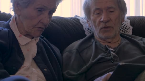 Two aging seniors talk while holding a mobile tablet - dolly shot - Filmati, video